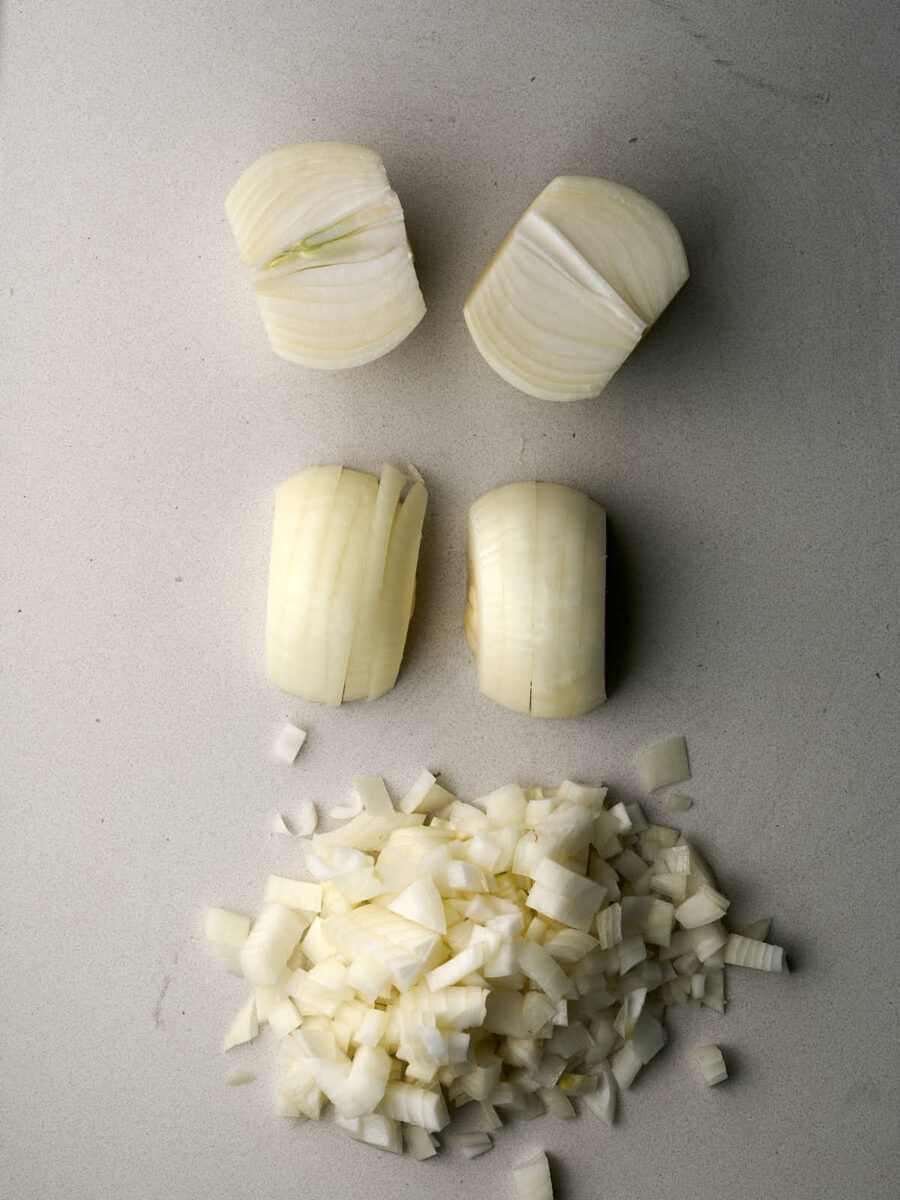 Raw onions in two halves and diced up finely on a white countertop.