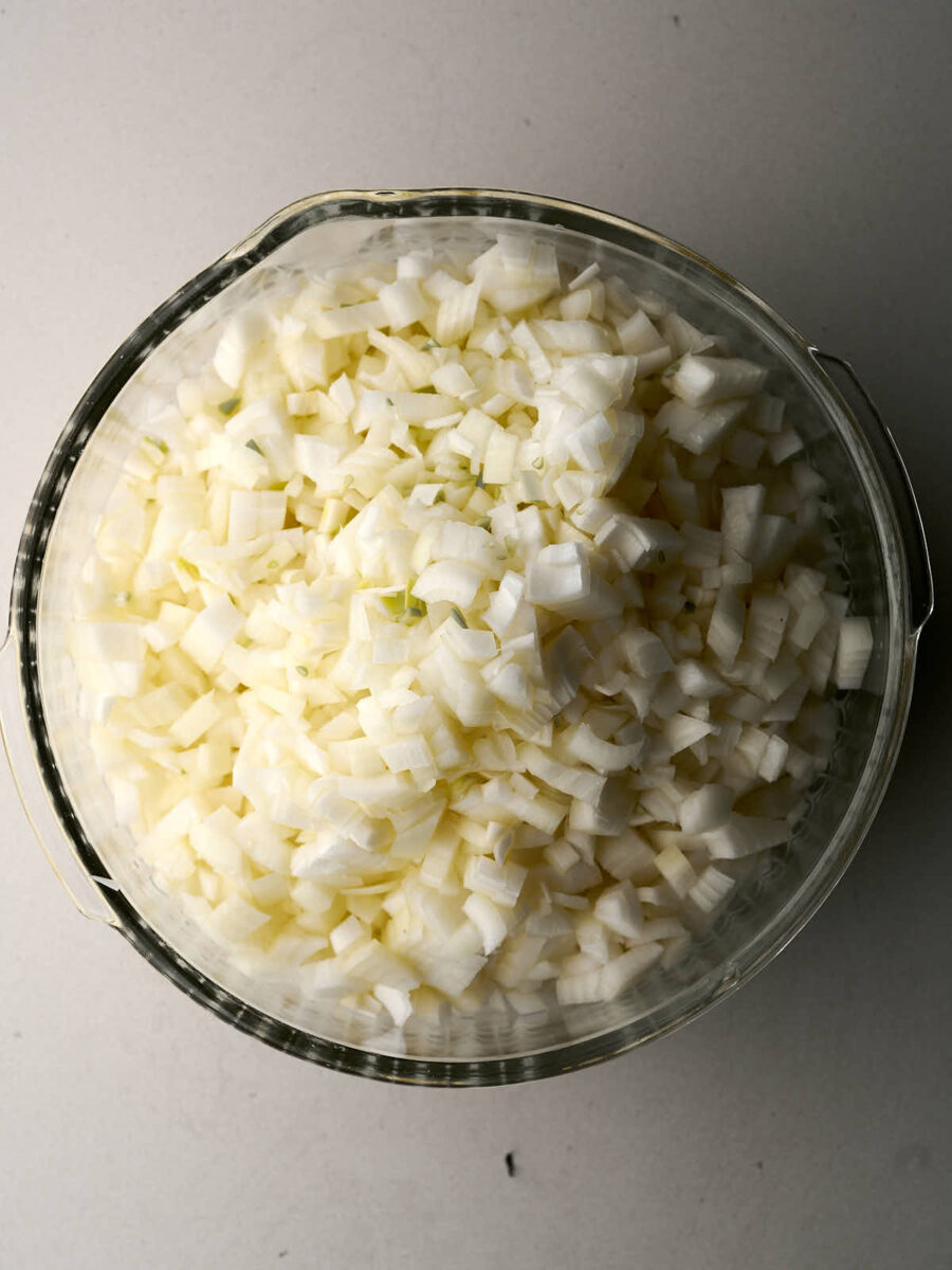 A big pile of diced onions in a glass bowl.