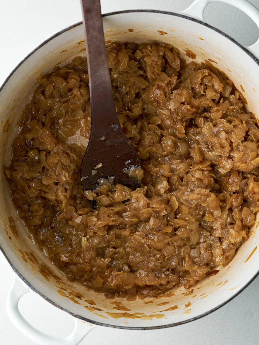 Caramelized onions cooking in a large pot with a wooden spoon.