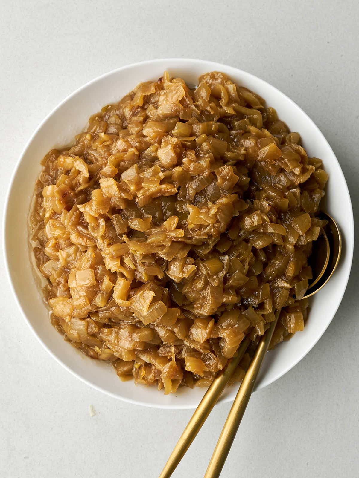 Caramelized onions in a white bowl with gold utensils.