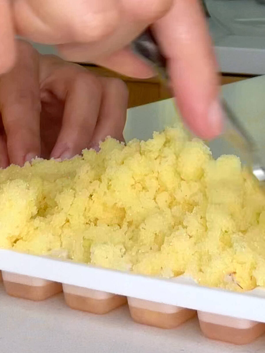 A mound of yellow sugar on a white and pink sugar cube mold.