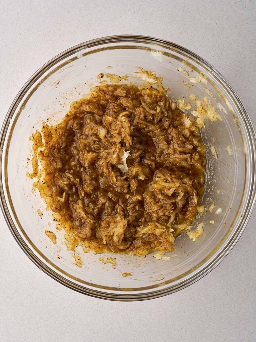 Spices and grated onion in a large glass bowl.