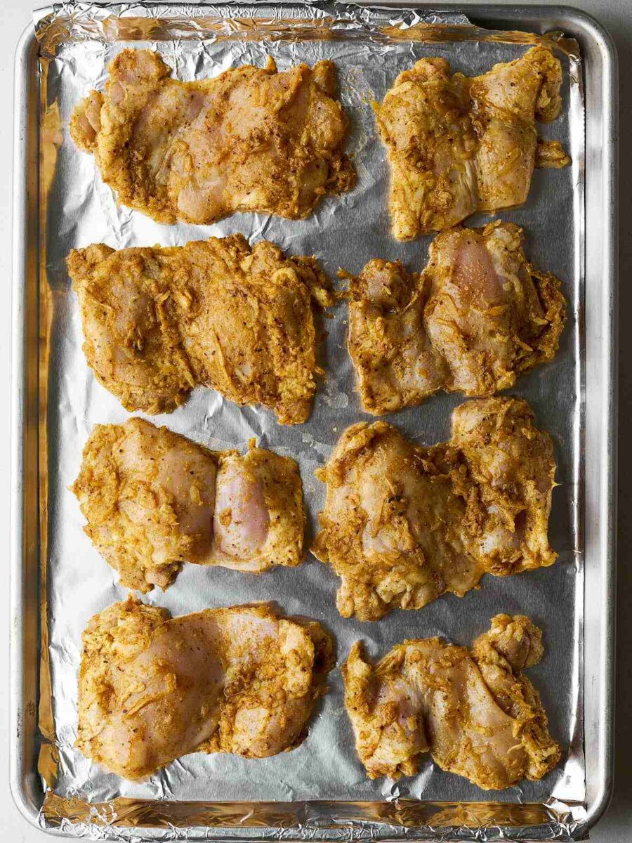 Raw, spiced chicken thighs laid out on a sheet pan with metal foil.