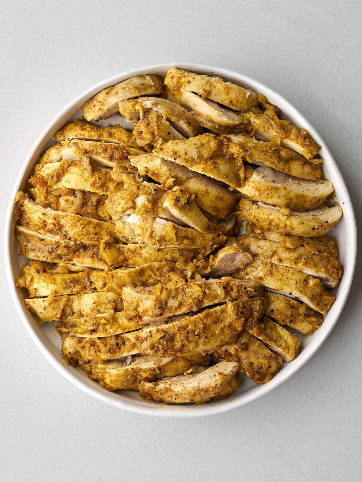 Sliced cooked chicken thighs on a large white plate.