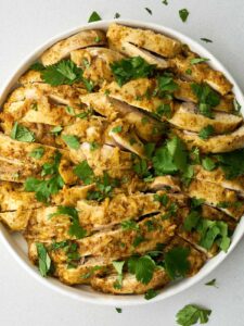 Sliced cooked chicken thighs on a large white plate with a green cilantro garnish.