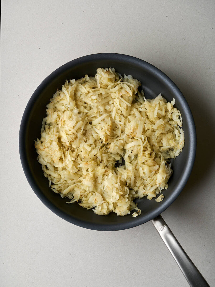 A black frying pan filled with finely shredded potatoes.