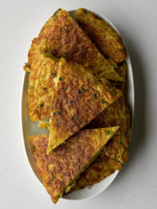 An oval white platter filled with slices of golden brown kuku (potato frittata), cut into triangular wedges.