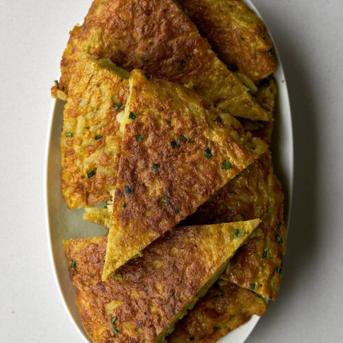 An oval white platter filled with slices of golden brown kuku (potato frittata), cut into triangular wedges.