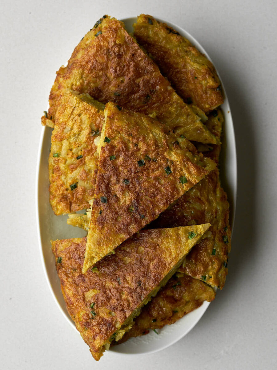 An oval white platter filled with slices of golden brown kuku (potato frittata), cut into triangular wedges.
