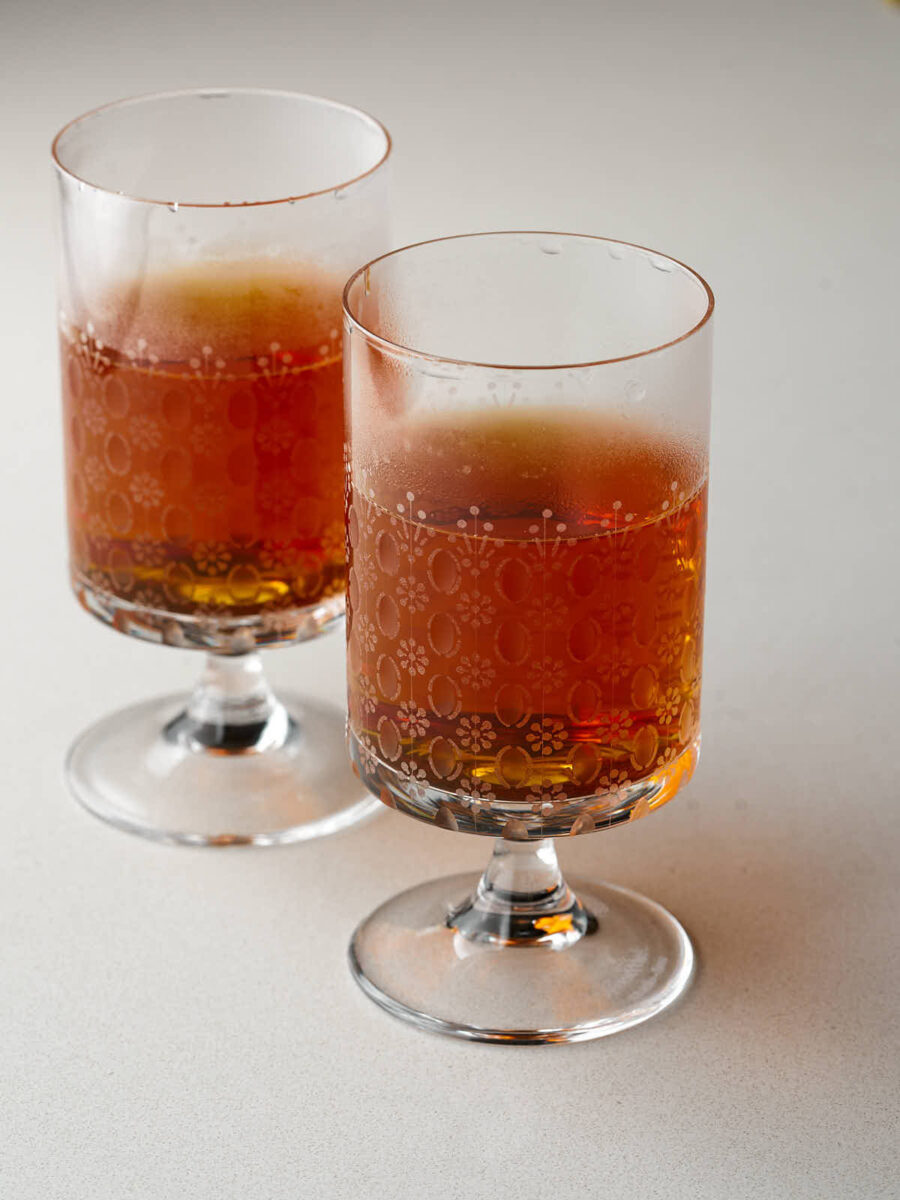 Two clear, footed glasses with etched floral patterns, each filled with dark amber tea. Condensation is visible on the outside of the glasses.