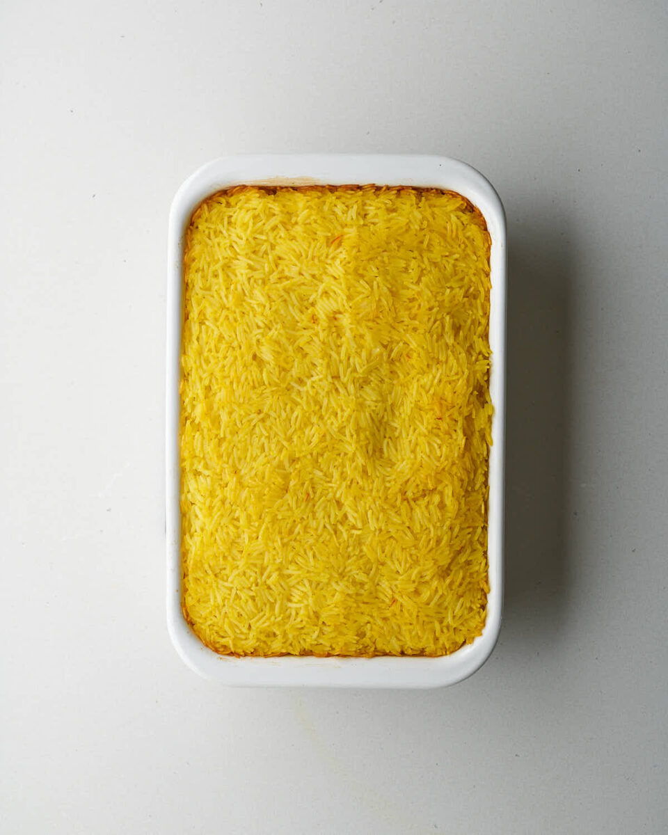 An overhead shot of a white rectangular baking dish filled with bright yellow rice that has been cooked and is slightly golden brown around the edges.