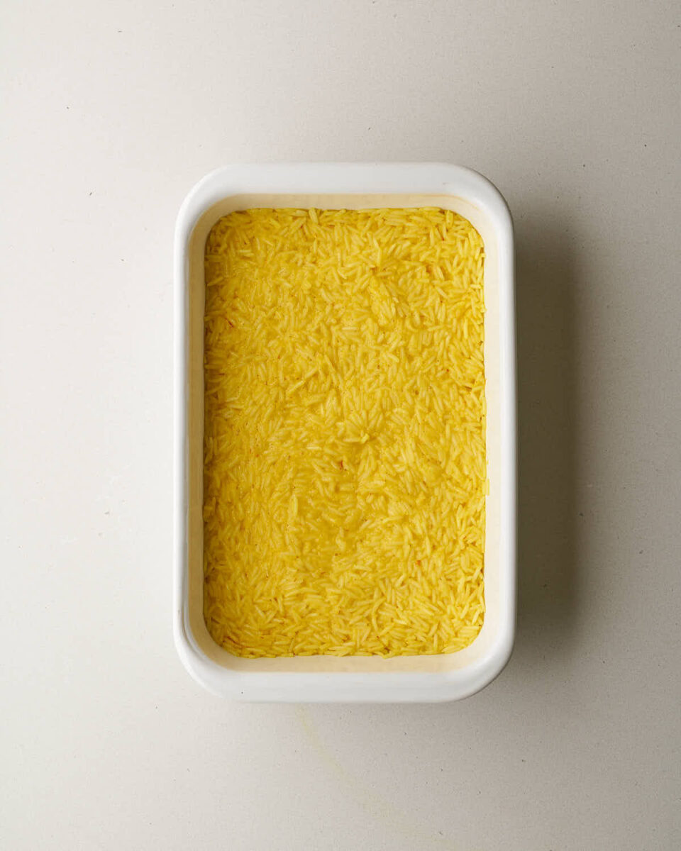 An overhead shot of a white rectangular baking dish filled with a layer of yellow rice.
