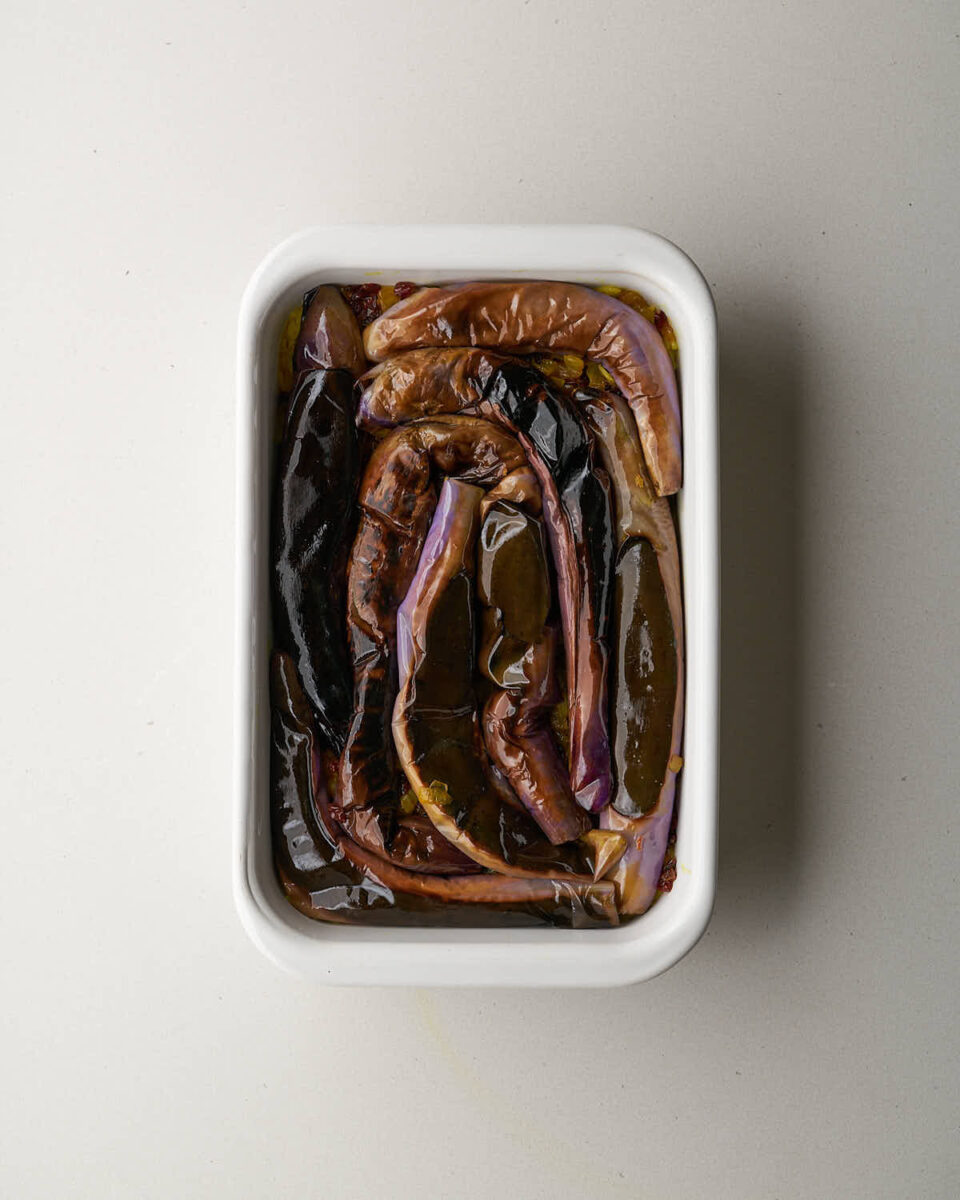 An overhead shot of a white rectangular baking dish. A layer of yellow rice is topped with cooked onions, barberries, and then a layer of roasted eggplant slices.