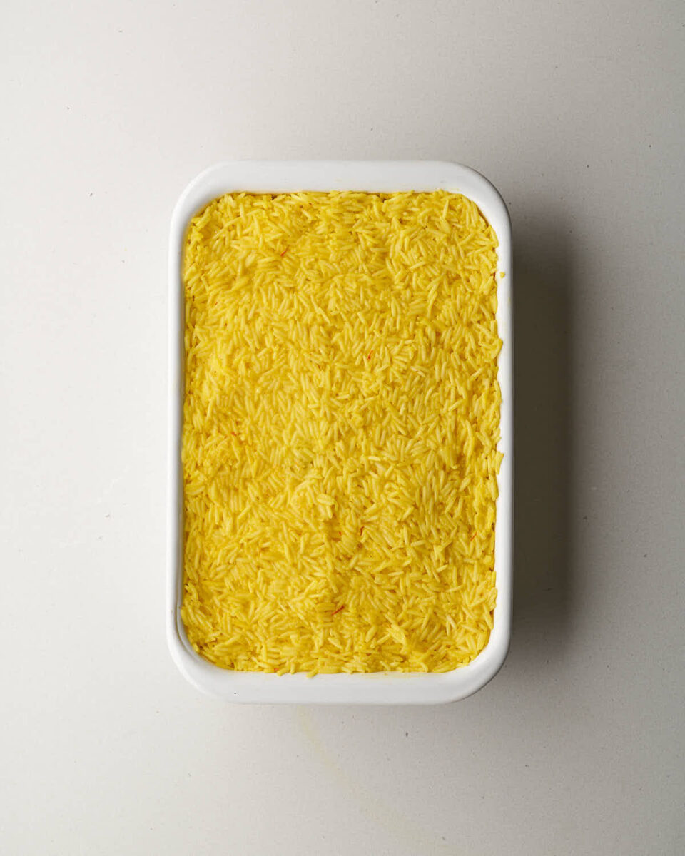 An overhead shot of a white rectangular baking dish filled with a layer of yellow rice.