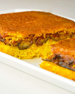 A rice casserole dish filled with bright yellow rice and eggplant that has been cut in half and baked until crispy and brown.