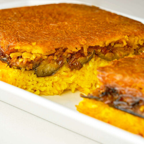 A rice casserole dish filled with bright yellow rice and eggplant that has been cut in half and baked until crispy and brown.