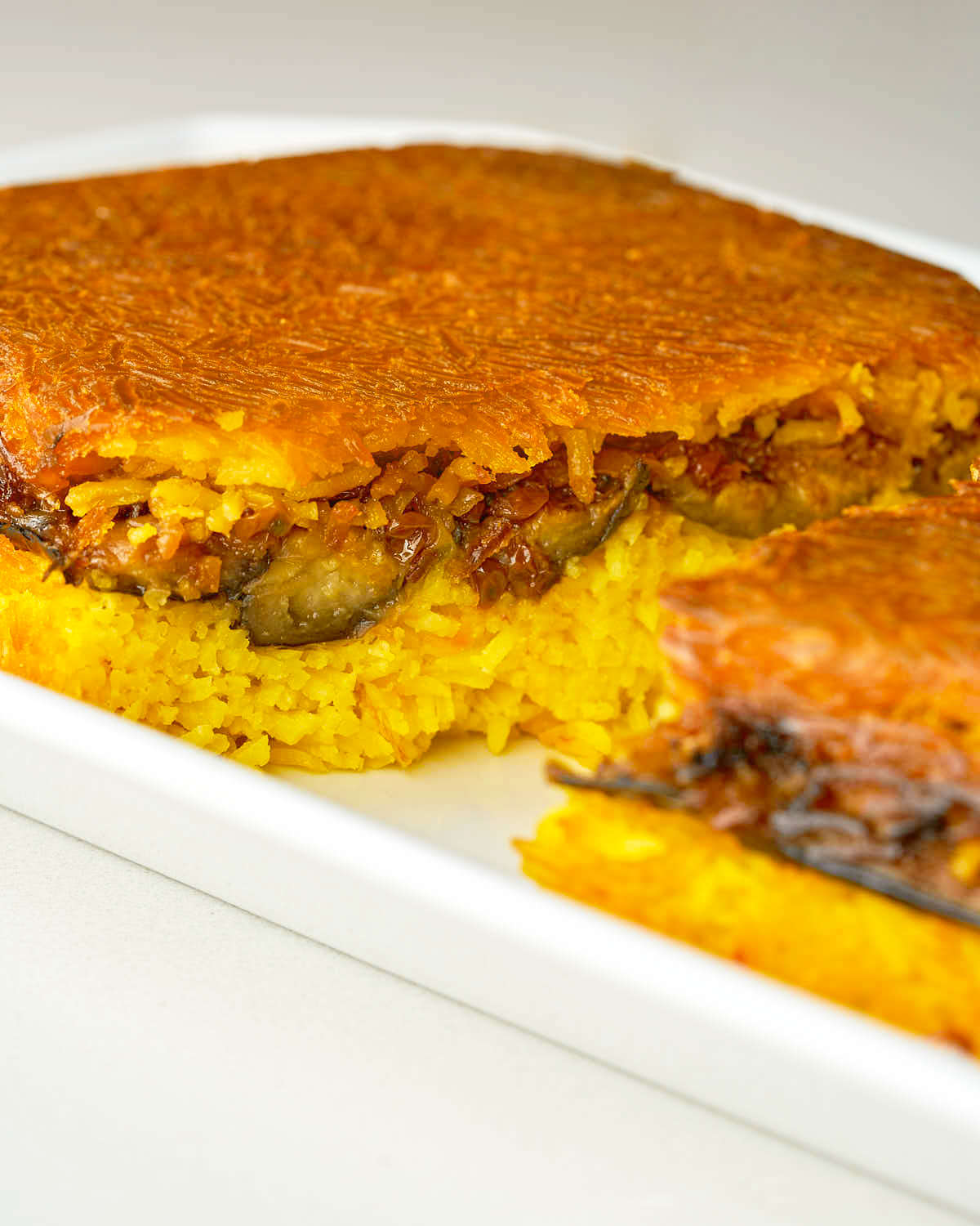 A rice casserole dish filled with bright yellow rice and eggplant that has been cut in half and baked until crispy and brown.
