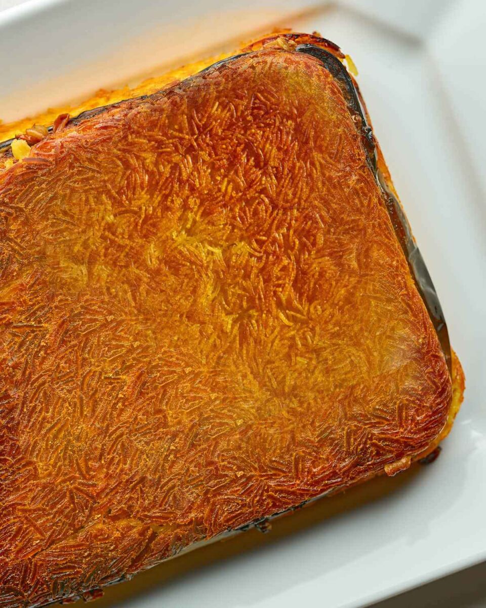 A rice casserole dish filled with bright yellow rice and eggplant that has been baked until crispy and brown and flipped onto a white platter.