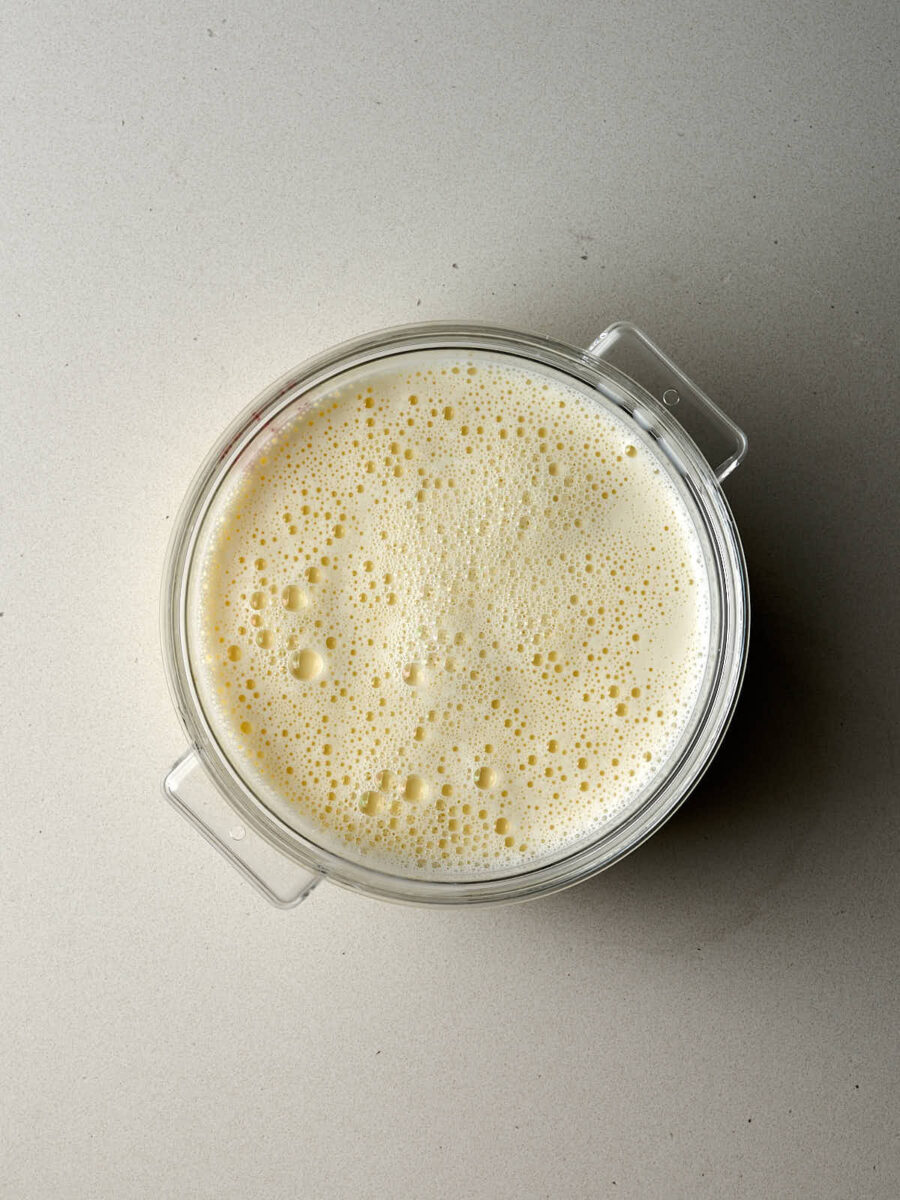 An overhead shot of a plastic tub containing a pale yellow, frothy liquid. The surface is covered in tiny bubbles.