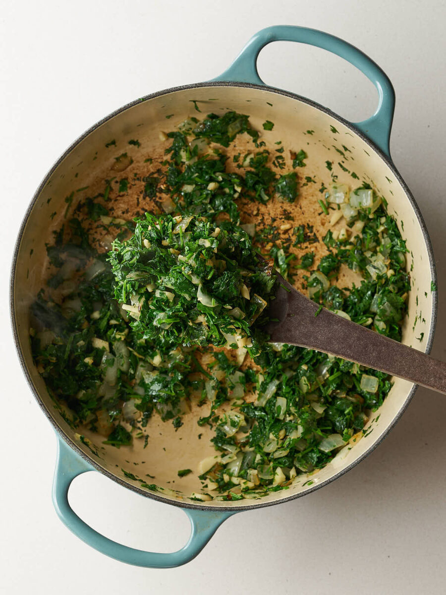 Chopped herbs and garlic sautéing with onions in a light blue dutch oven.