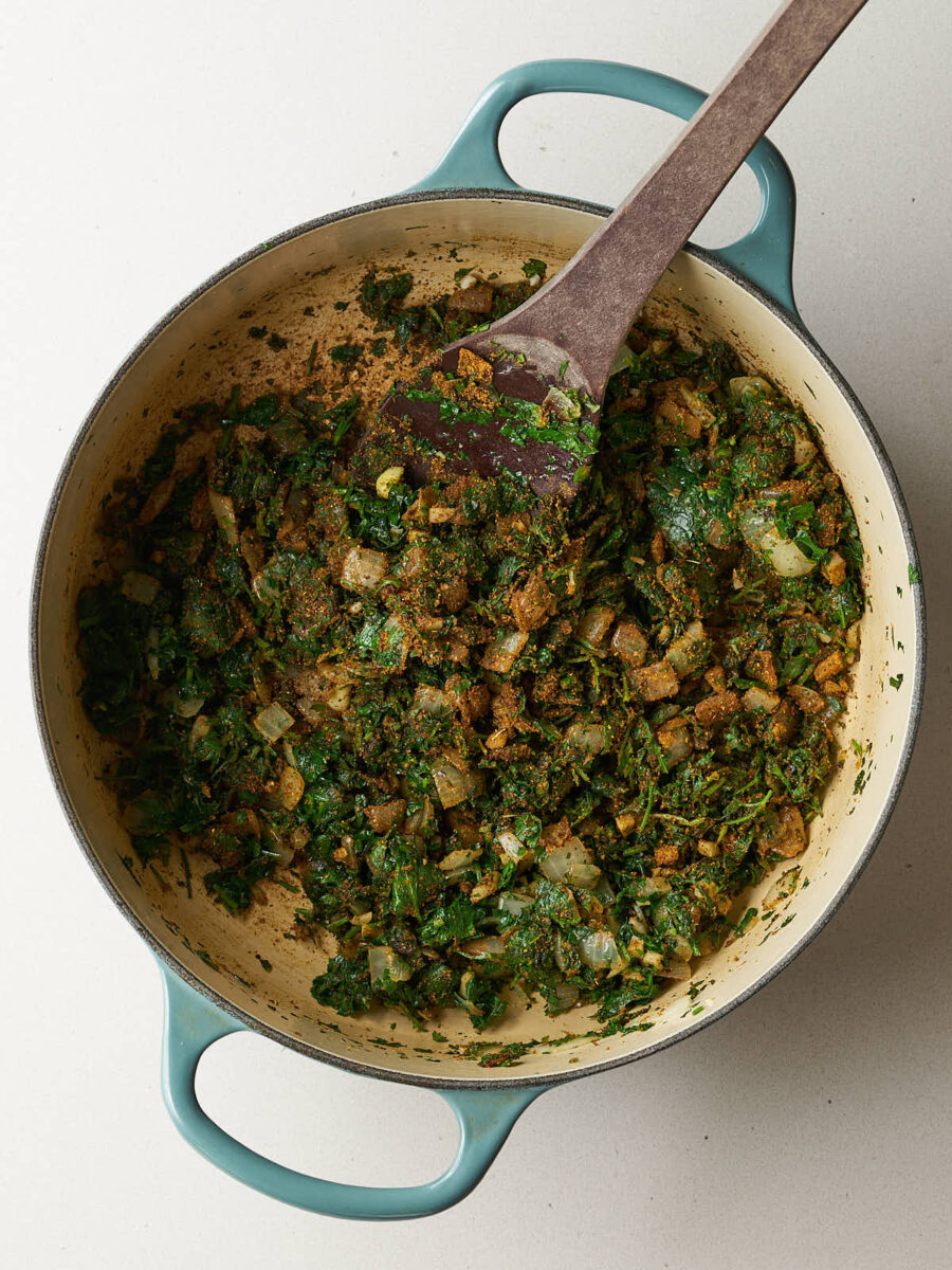 Spices, herbs, garlic, and onions being stirred together in a light blue dutch oven.