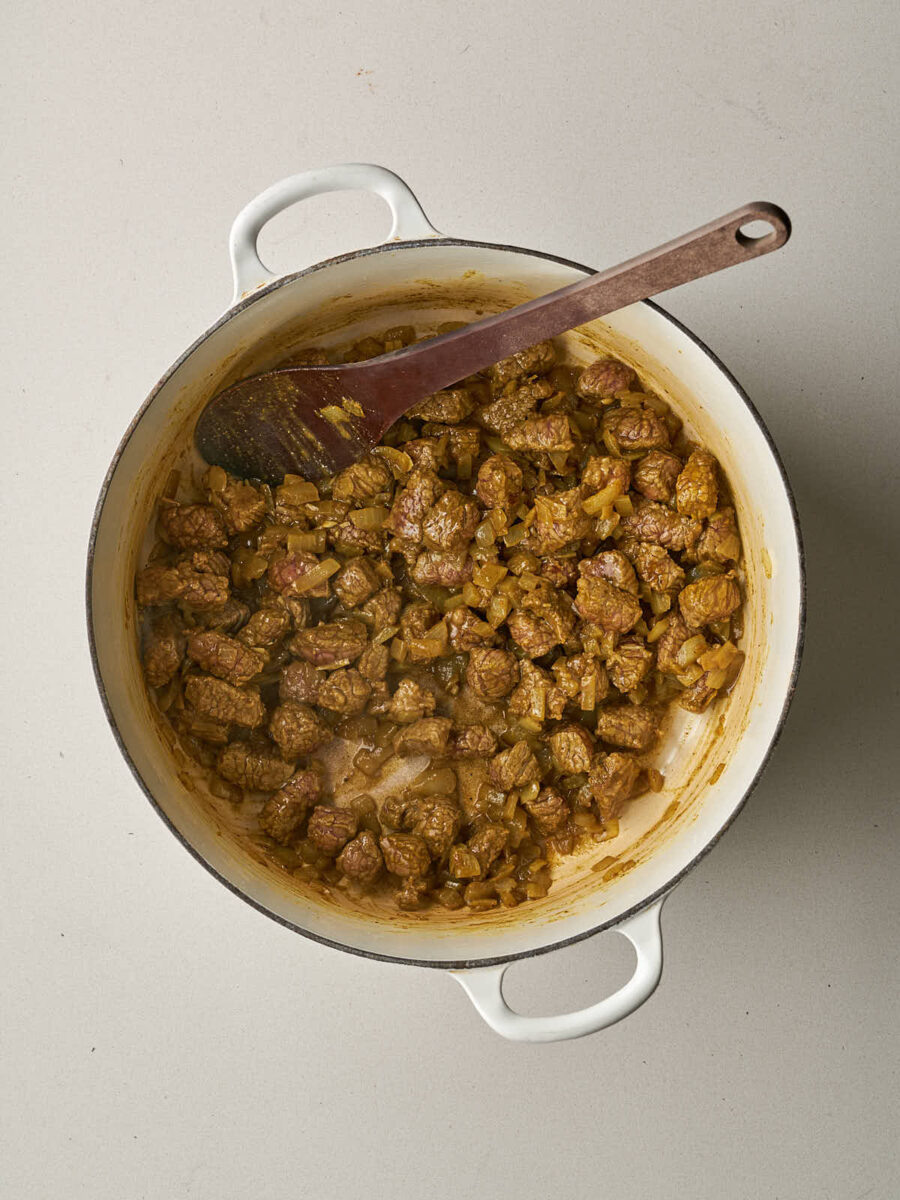 The meat and onions are well-combined and browned with spices in the Dutch oven.