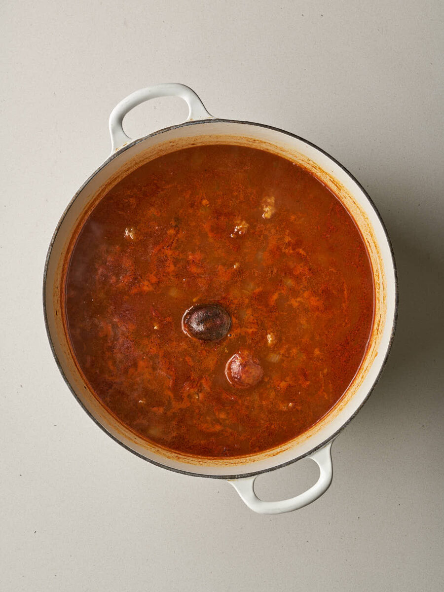 A reddish broth simmering in the pot with two whole dried limes floating on the surface.