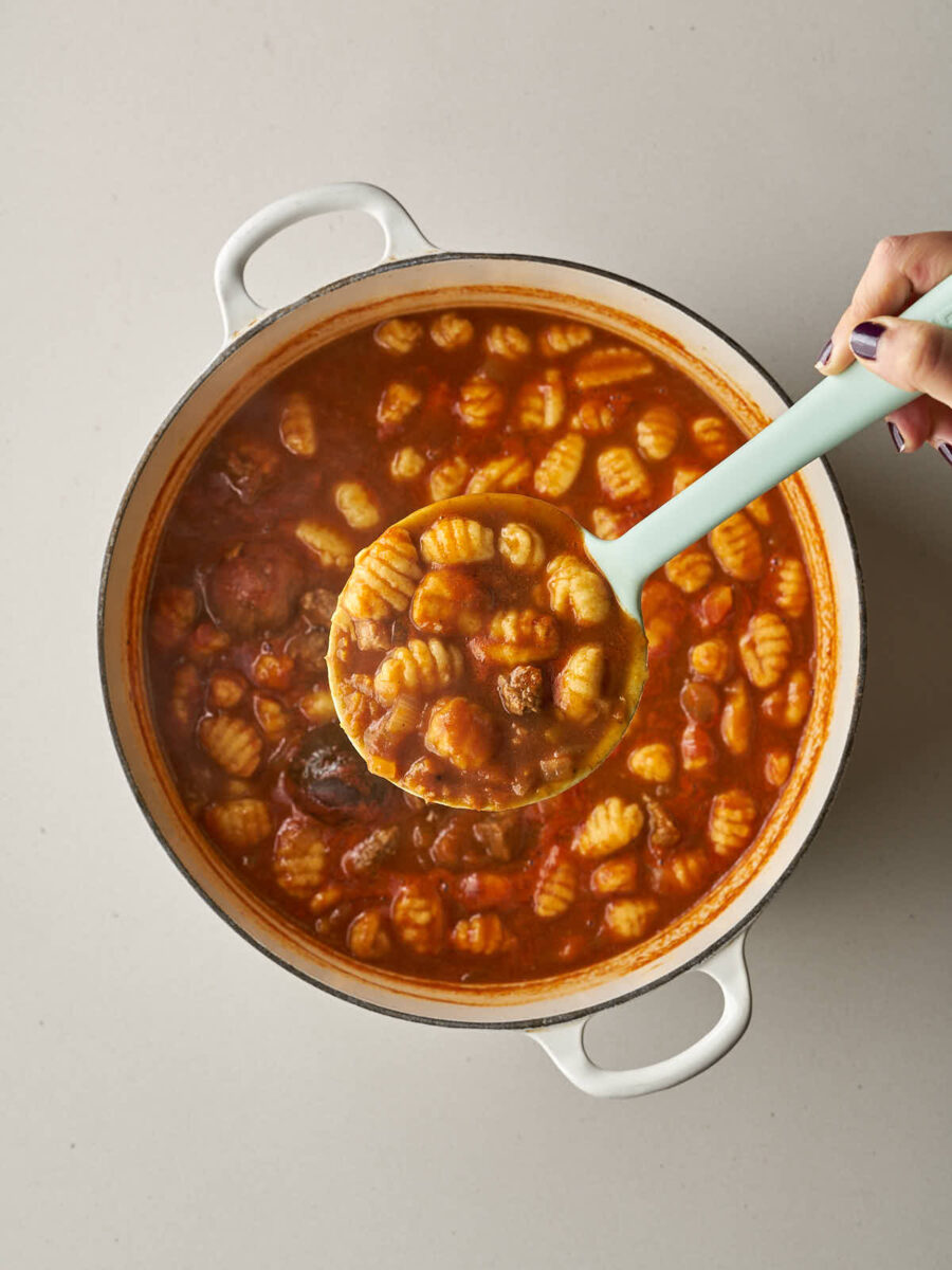 A light blue ladle scooping a serving of the finished gnocchi and meat stew from the pot.