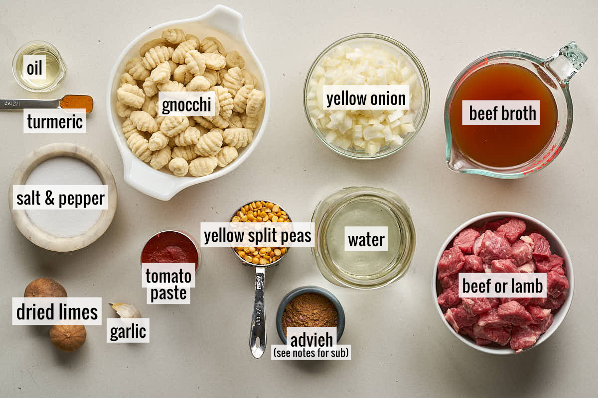 A top-down view of labeled ingredients for Gheymeh Gnocchi, including gnocchi, chopped onions, beef broth, cubed meat, yellow split peas, tomato paste, dried limes, and various spices.