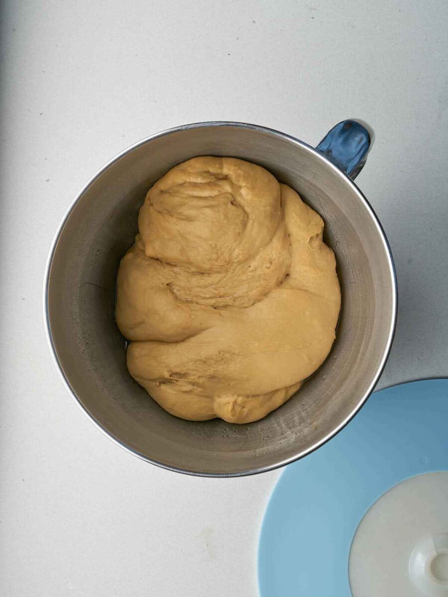 The bagel dough has risen, filling more of the stainless steel mixing bowl. A blue lid is visible on the side.