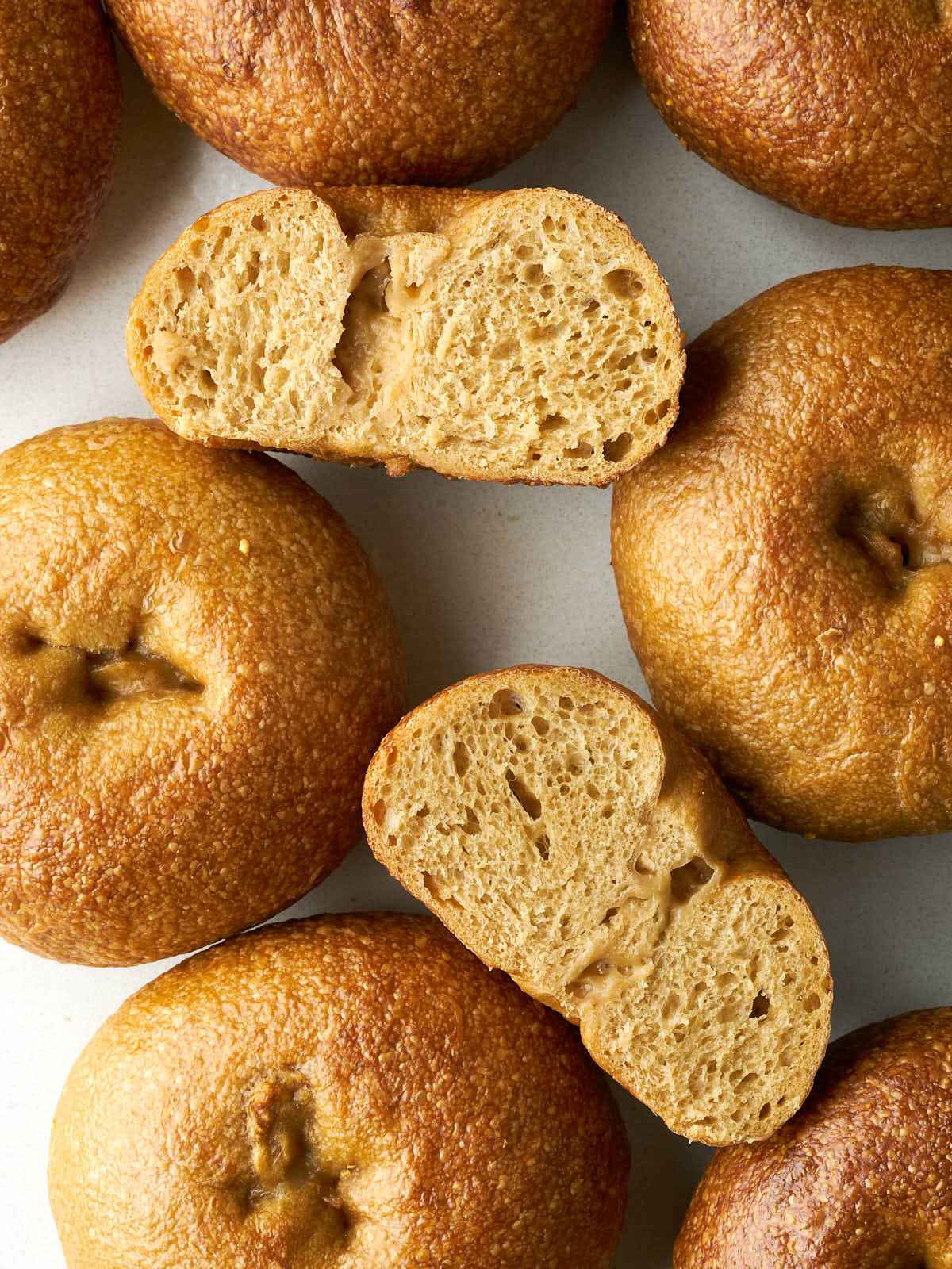 A top-down view of several baked bagels scattered on a white surface, with two sliced in half to show the crumb.