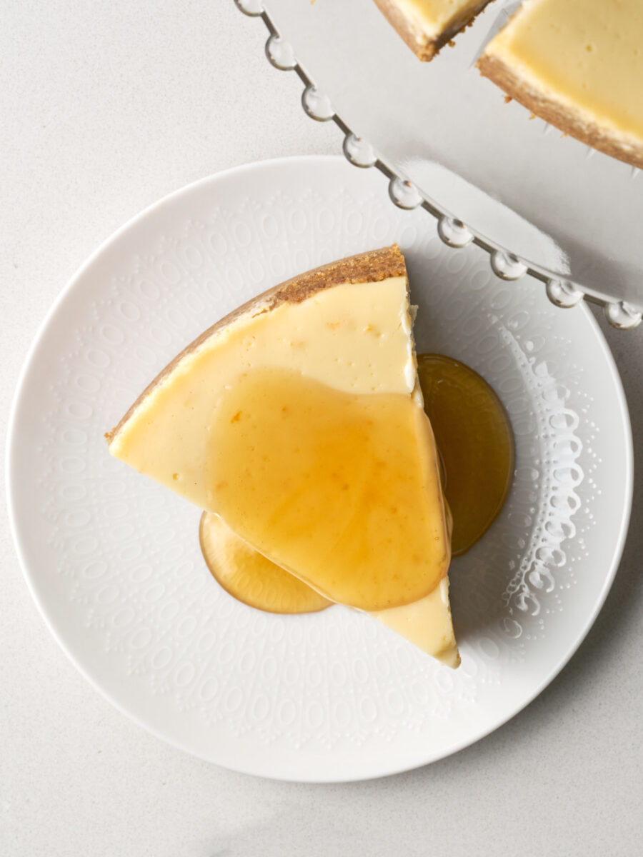 Overhead view of a slice of cheesecake topped with a generous layer of clear honey glaze on a white plate.