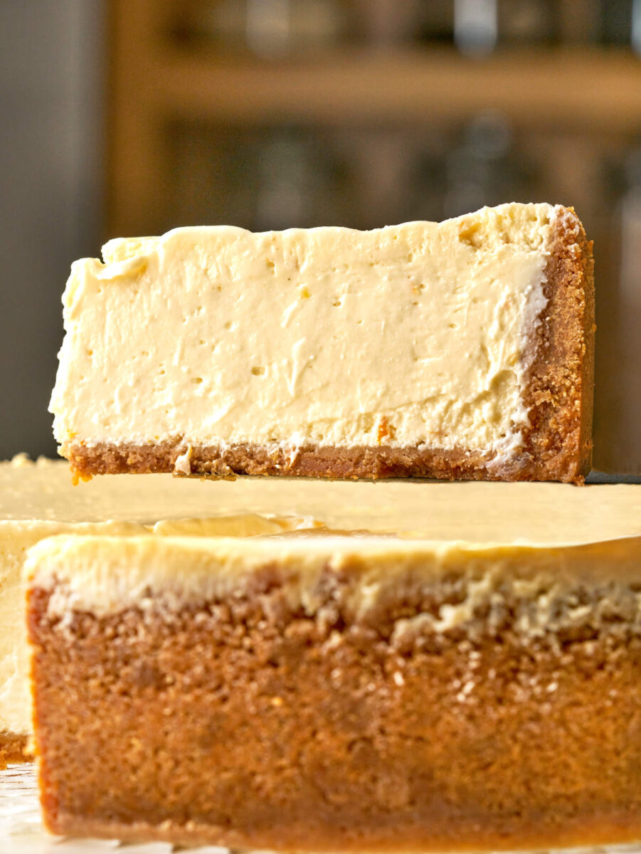 Close-up profile view showing a thick slice of creamy cheesecake being lifted off the whole cake with a server.