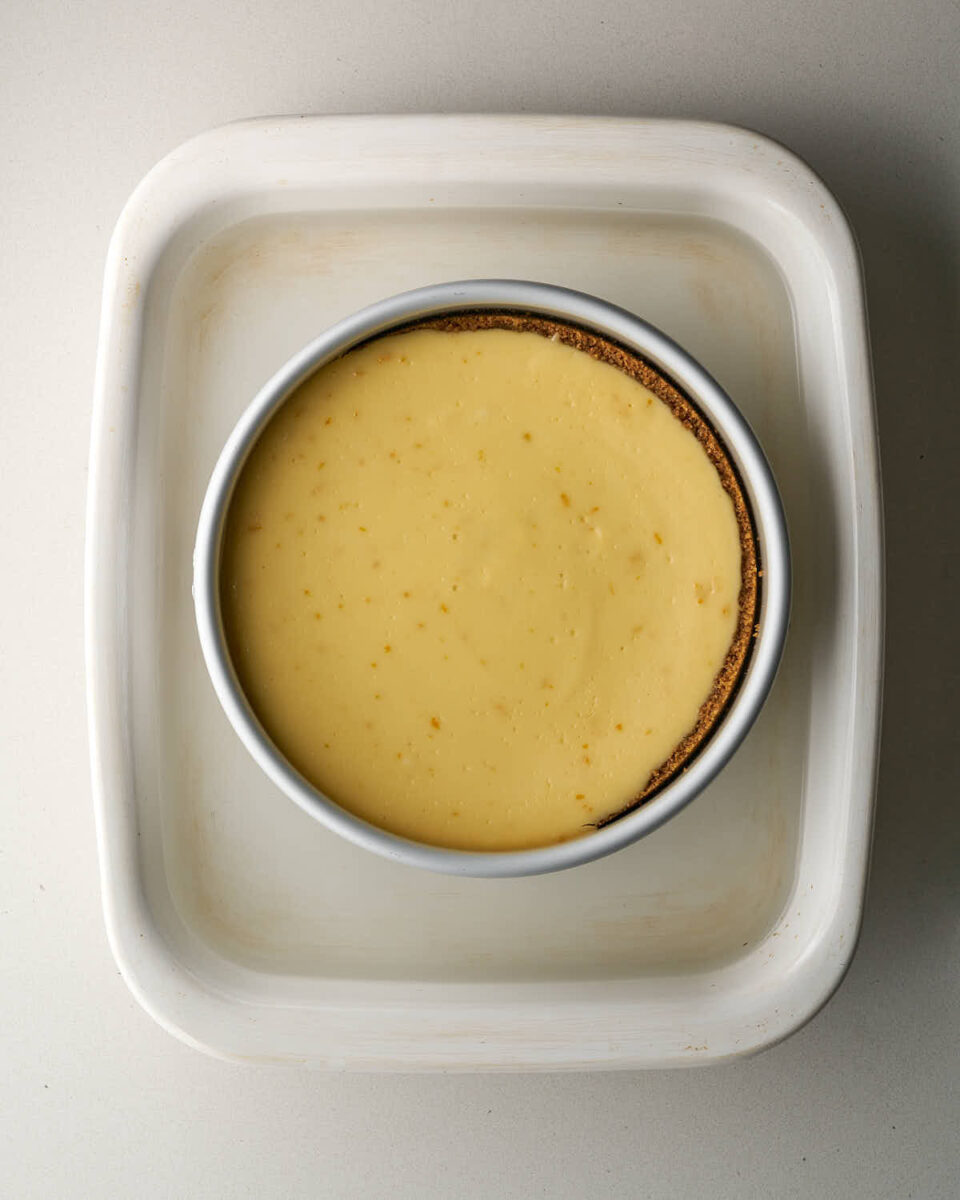 Overhead view of the fully baked, set cheesecake sitting inside the water bath in a white baking dish.
