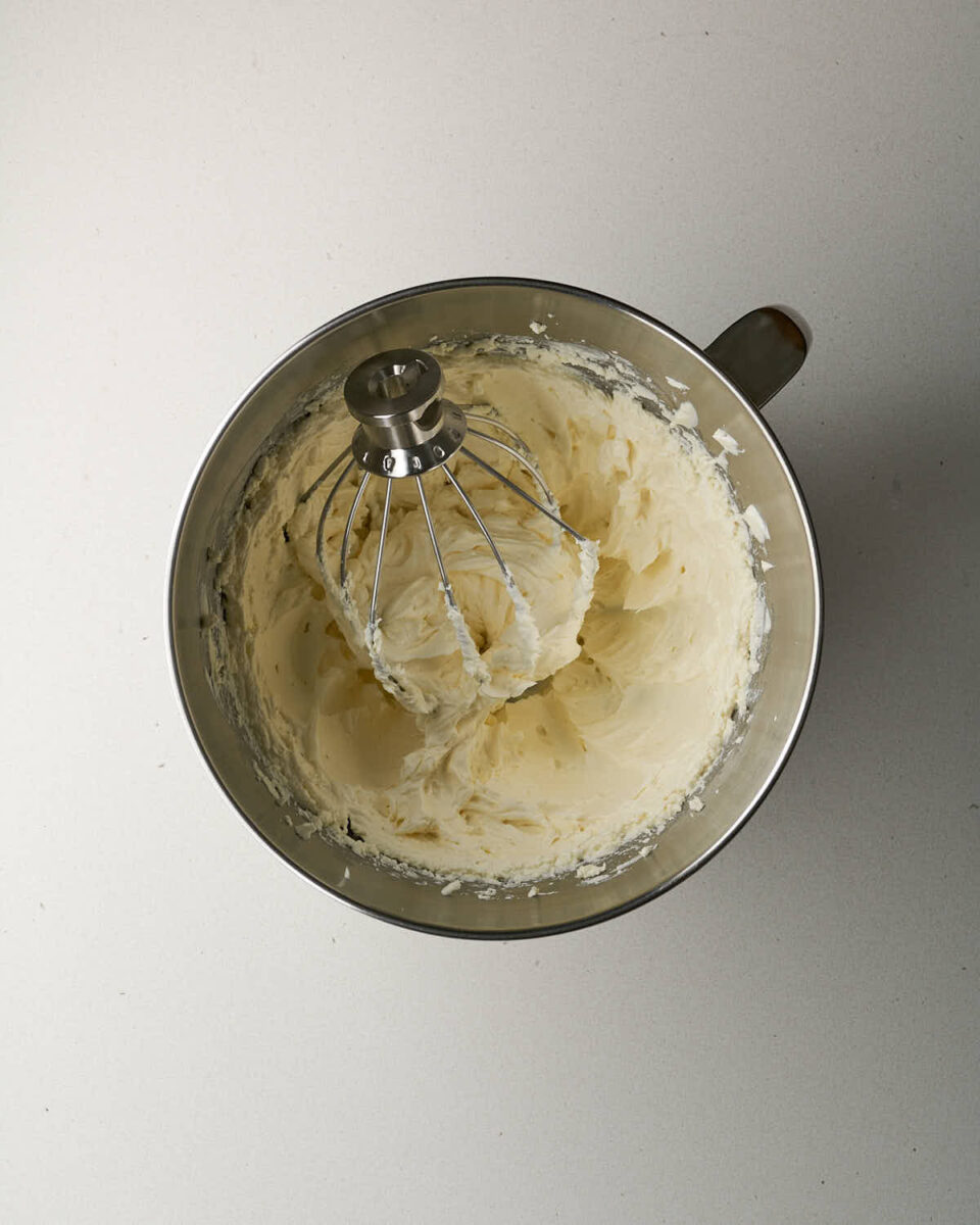 Top-down view of whipped cream cheese batter inside a metal stand mixer bowl with the wire whisk attachment.