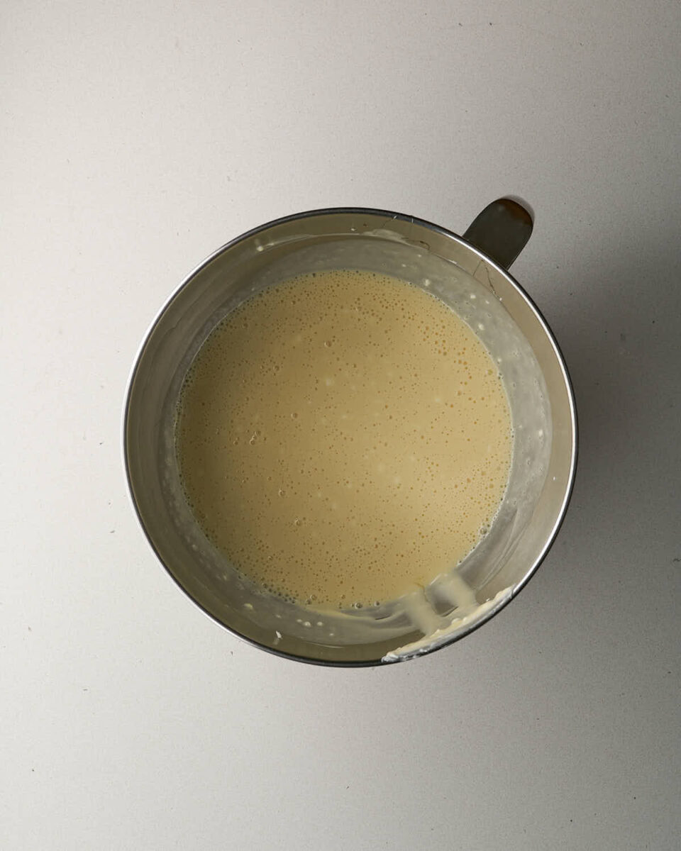 Overhead view of smooth, pale yellow cheesecake batter in a metal mixing bowl.