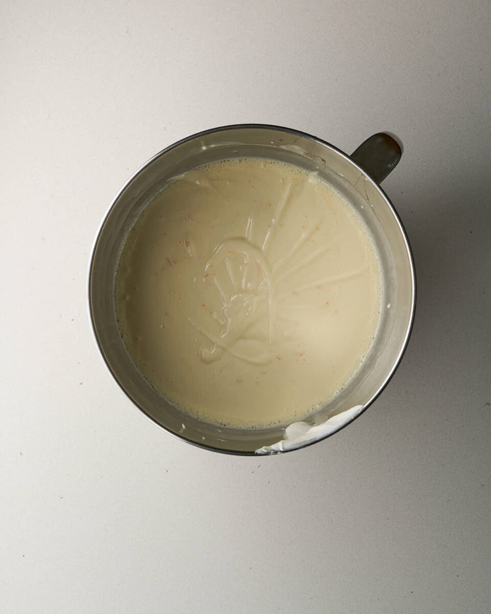 Top-down view of cheesecake batter with visible specks of orange zest mixed inside a stainless steel bowl.