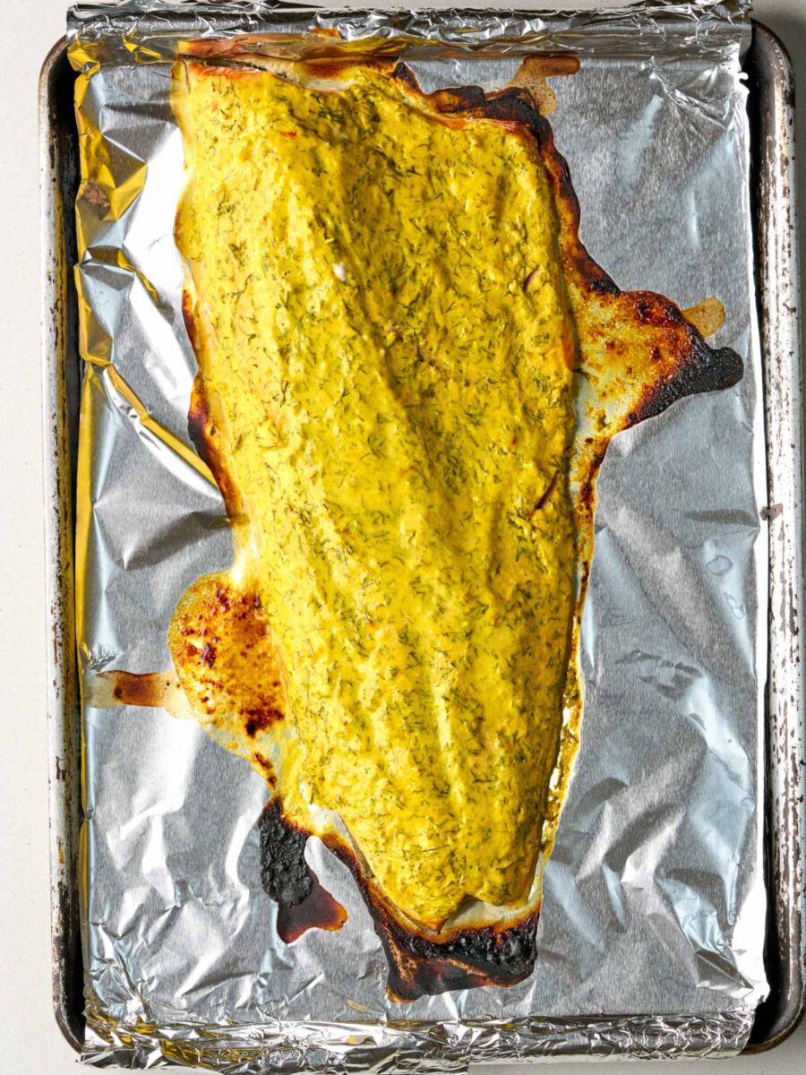 Baked salmon side on a foil-lined baking tray with a browned herb crust around the edges.