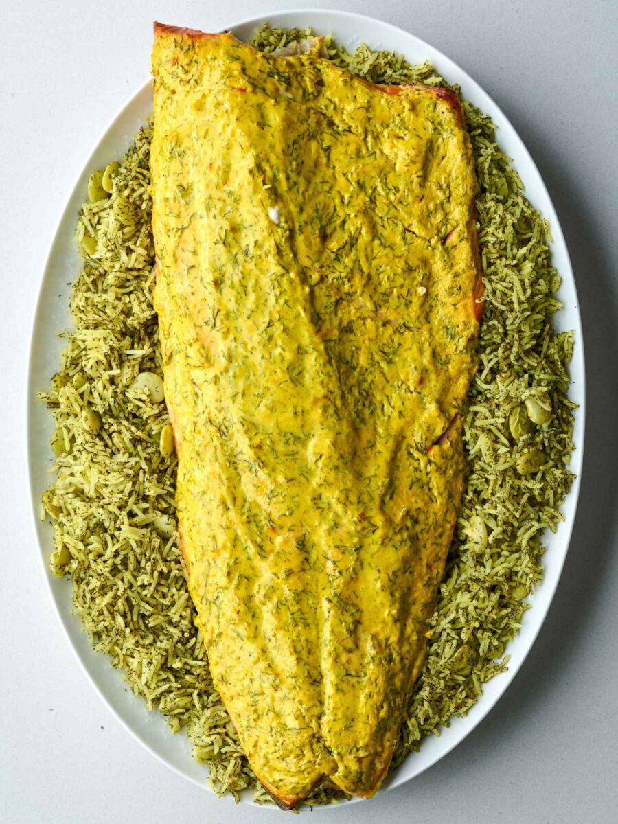 Whole baked salmon side topped with herb sauce, presented over a bed of green dill rice on a large oval platter.
