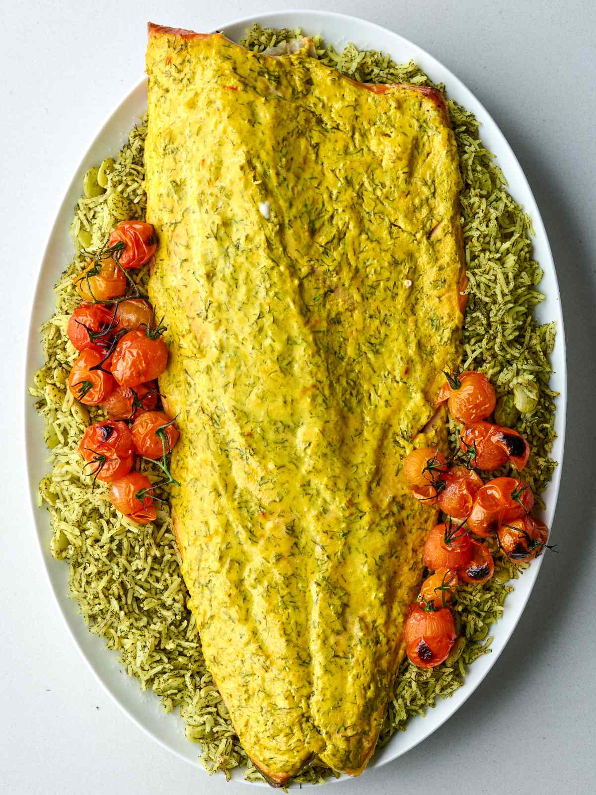 Baked salmon side on a bed of green rice, garnished with roasted cherry tomatoes on the vine.
