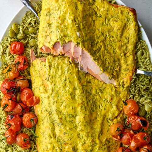 Serving forks breaking into a filet of baked salmon over dill rice and roasted tomatoes.