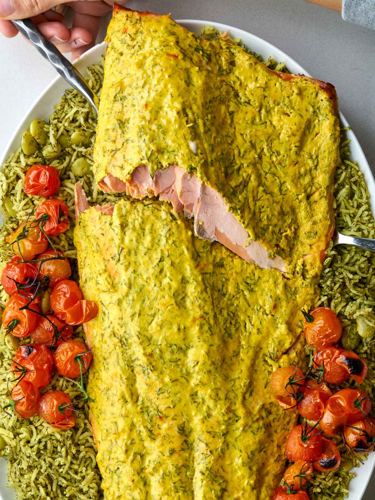 Serving forks breaking into a filet of baked salmon over dill rice and roasted tomatoes.